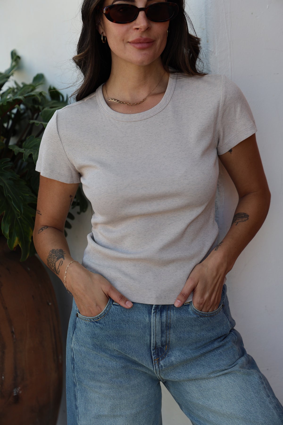 Person wearing a light gray t-shirt and blue jeans with sunglasses indoors.