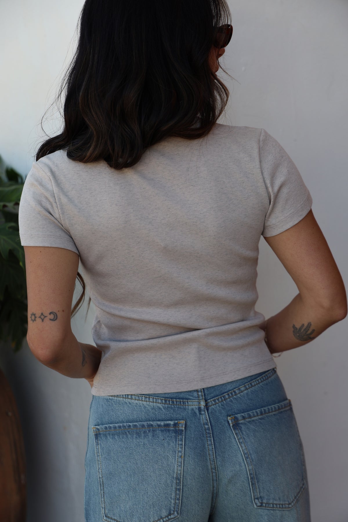 Person wearing a beige t-shirt and blue jeans against a white wall