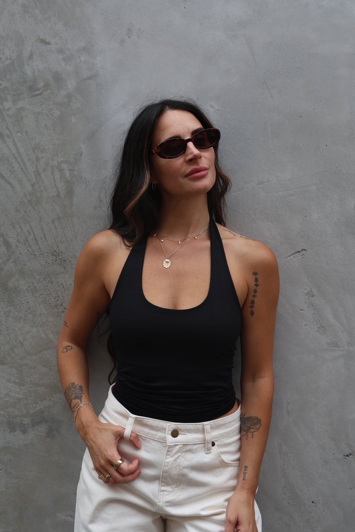 Woman wearing a black tank top and white pants against a gray wall