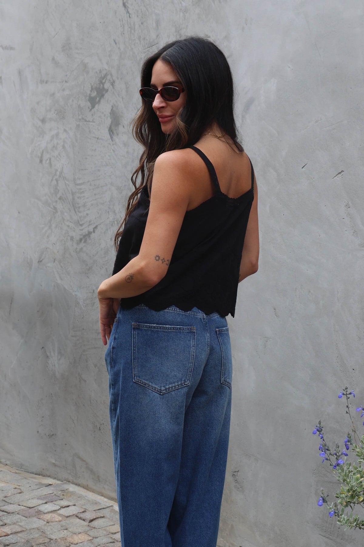 Woman wearing a black top and blue jeans against a gray wall.