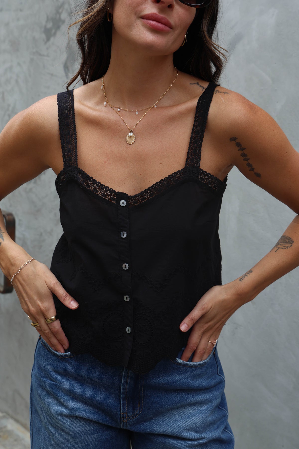 Woman wearing a black lace-trimmed top and blue jeans against a gray background