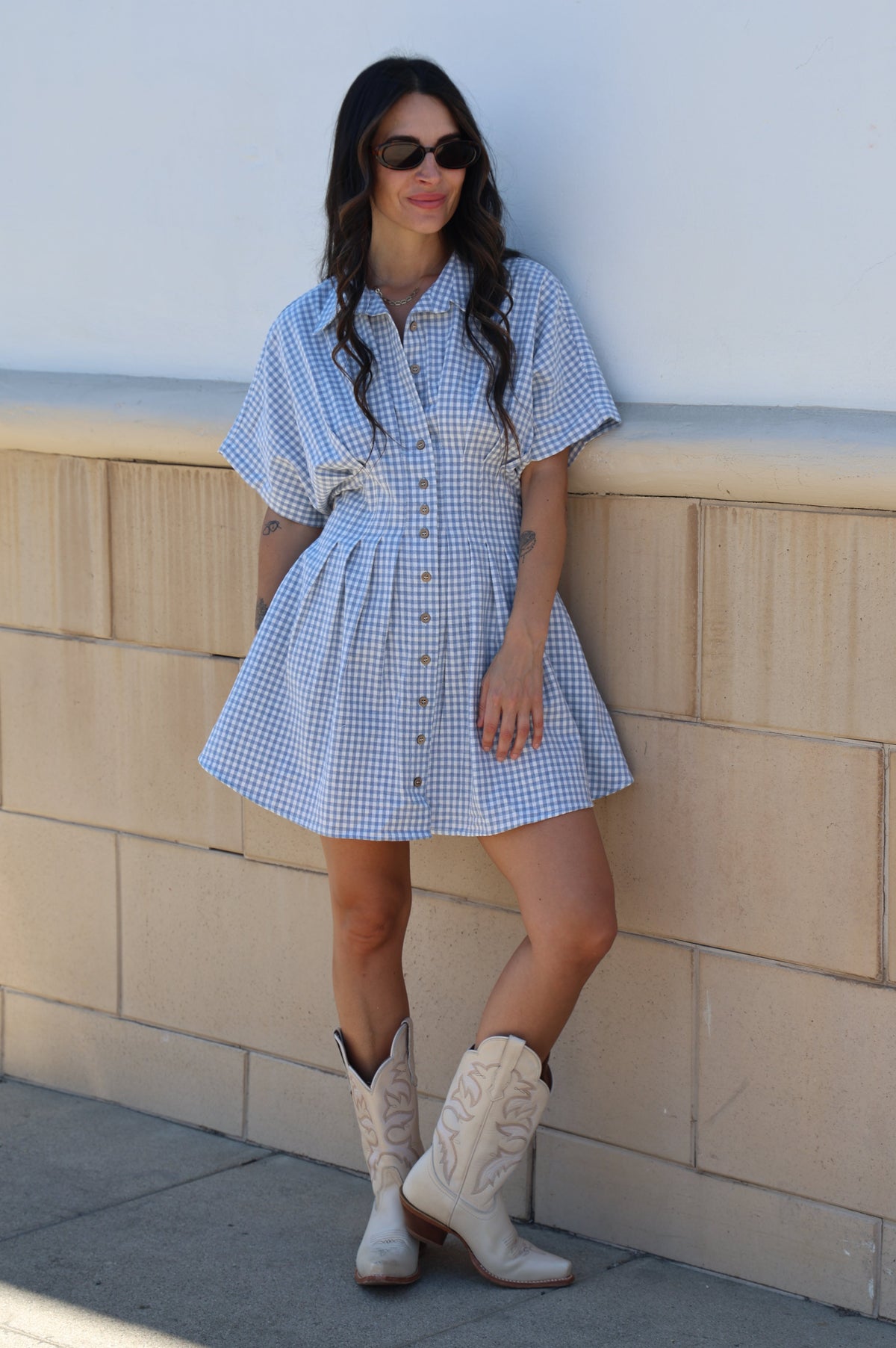 Woman in a blue checkered dress standing on a tiled floor.