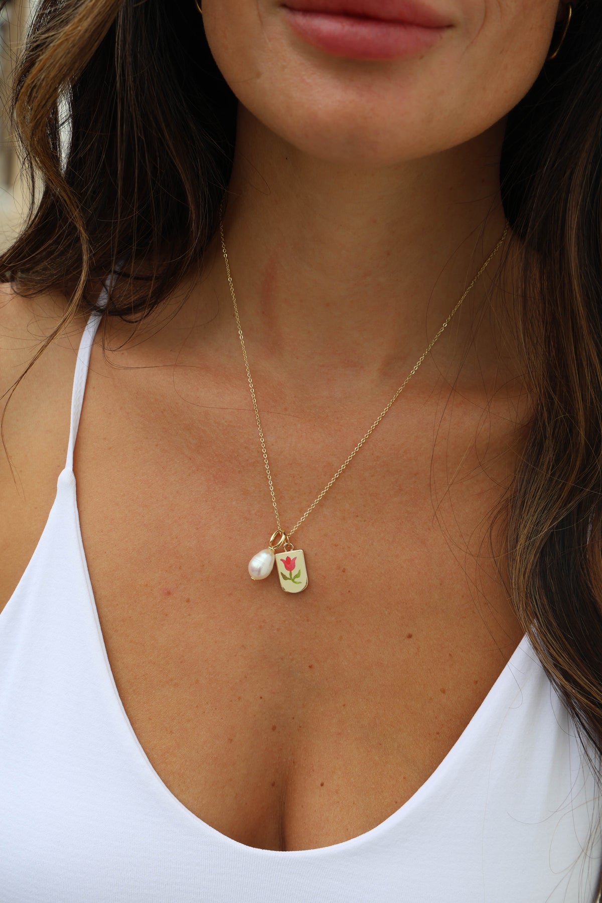 Close-up of a woman wearing a gold necklace with a pendant featuring a pearl and green leaf design.