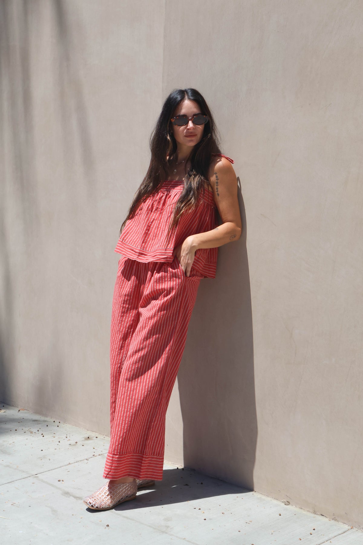 Woman in a red outfit leaning against a beige wall.