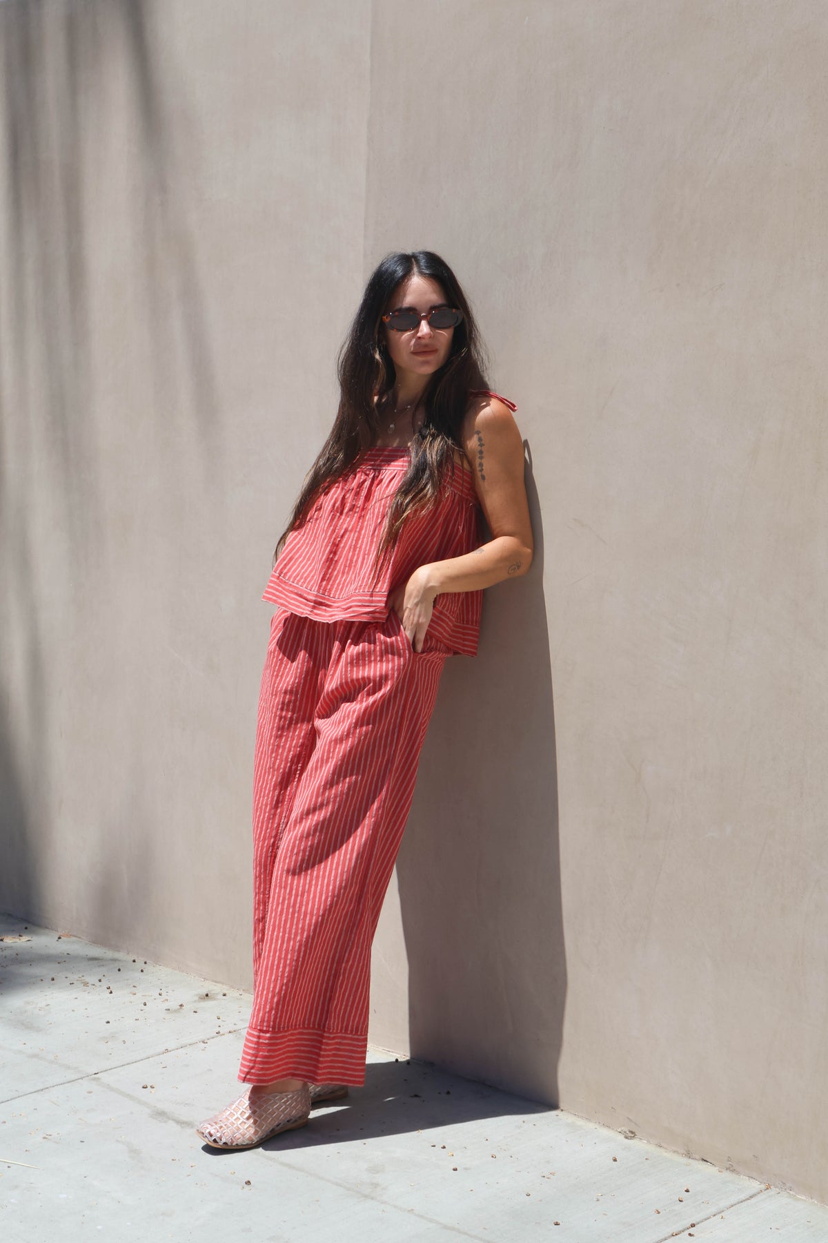 Woman in a red outfit leaning against a beige wall.