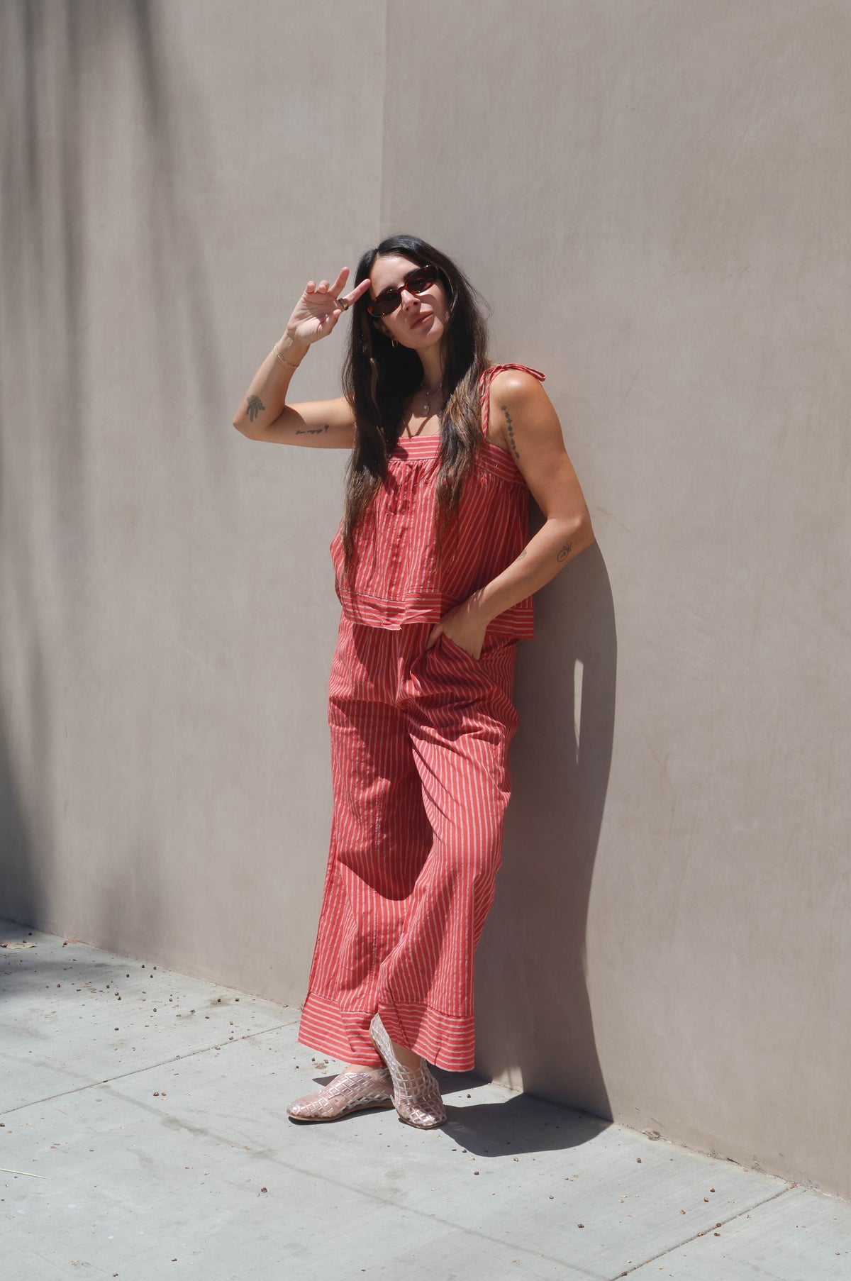 Woman in a red outfit standing against a beige wall on a sunny day.