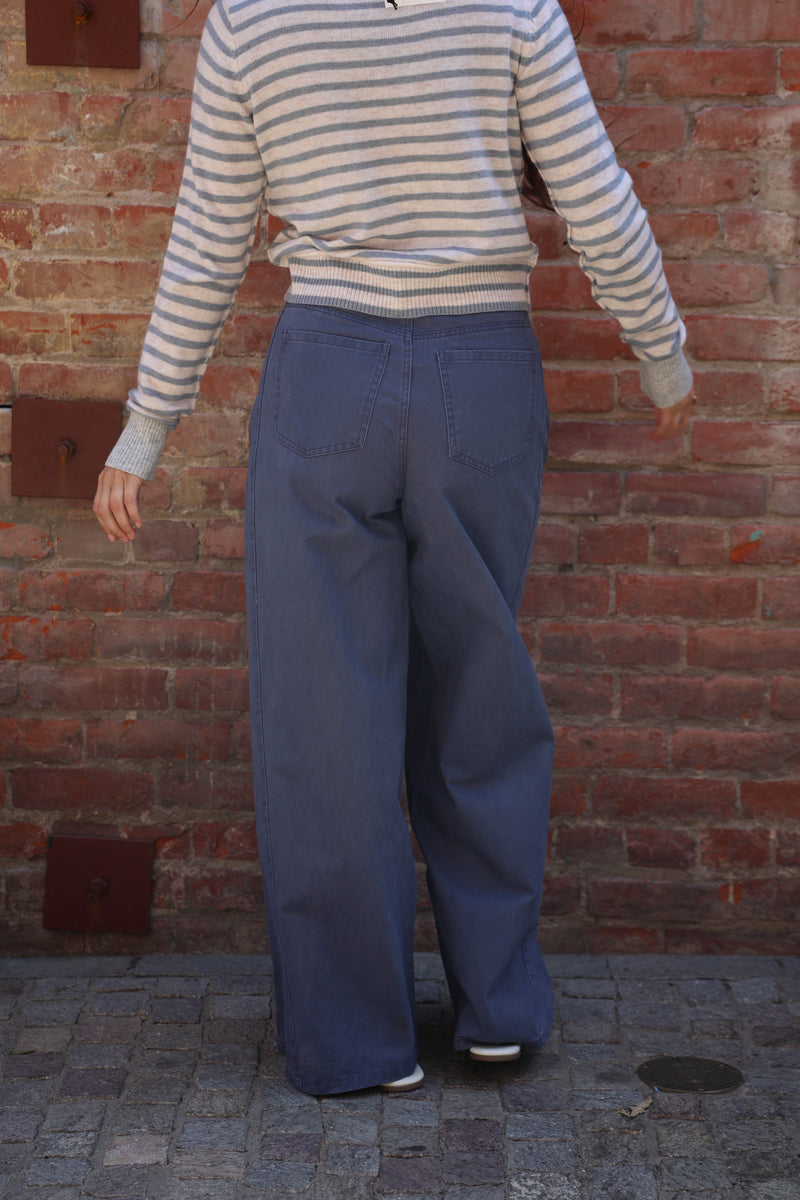 A person shown from behind wearing a cream and navy striped long-sleeve top and wide-leg blue jeans, standing against a red brick wall.