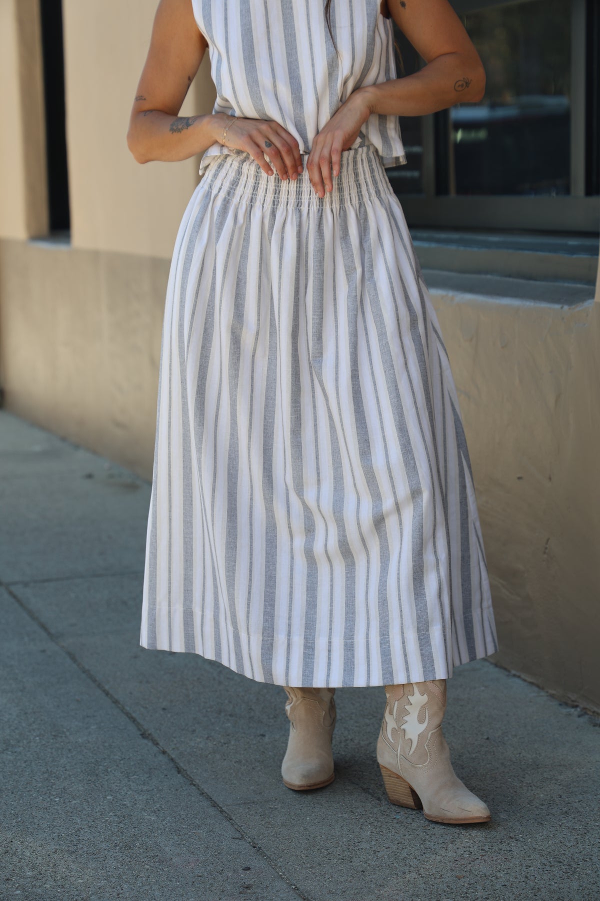 Person wearing a white dress with blue stripes, standing on a concrete surface.