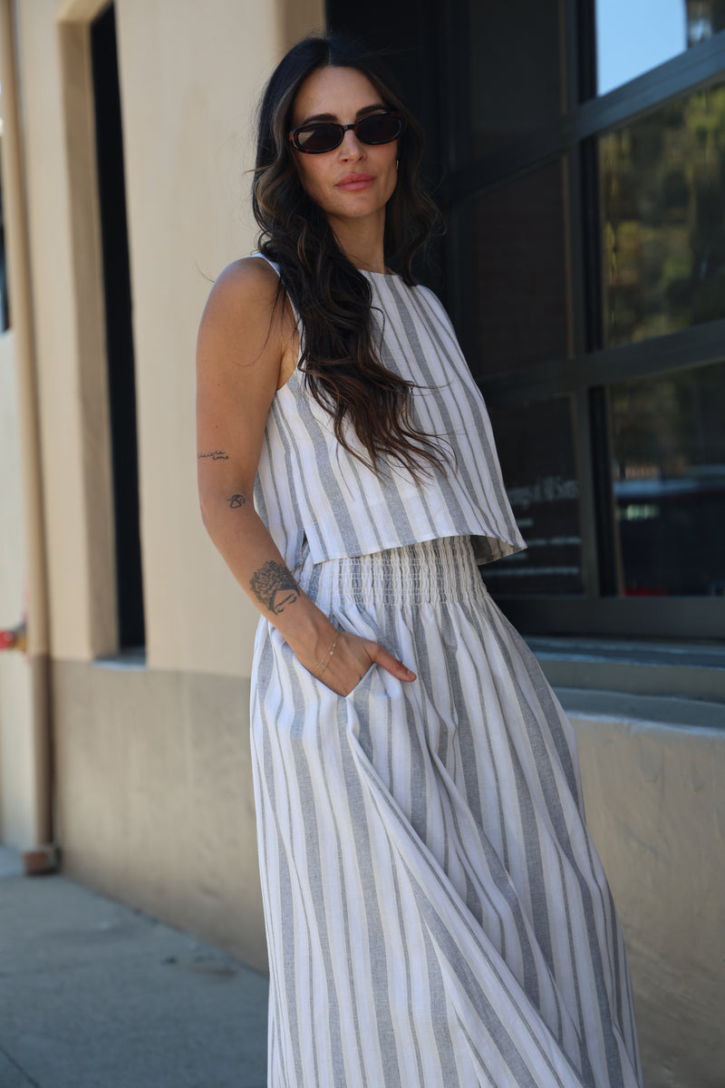 Woman wearing a striped dress and sunglasses, leaning against a wall.