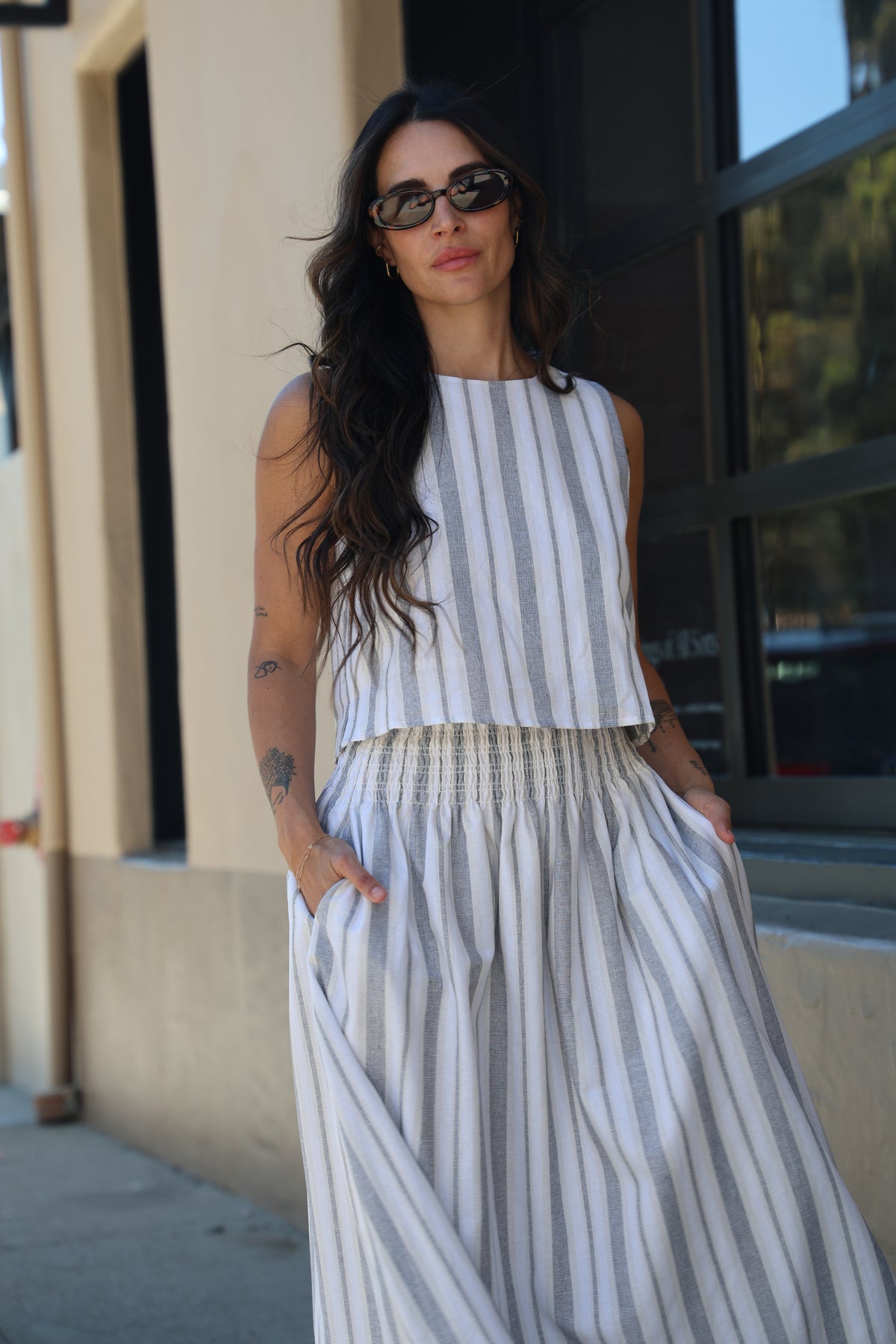 Woman wearing a striped dress and sunglasses, standing on a balcony.