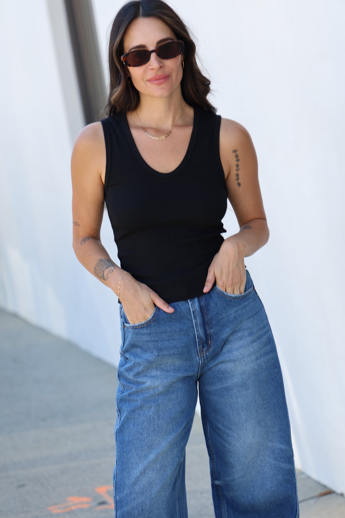 Person wearing a black sleeveless top and blue jeans on a white surface