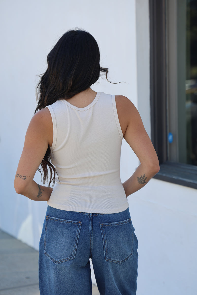 Person wearing a white sleeveless top and blue jeans standing on a car.