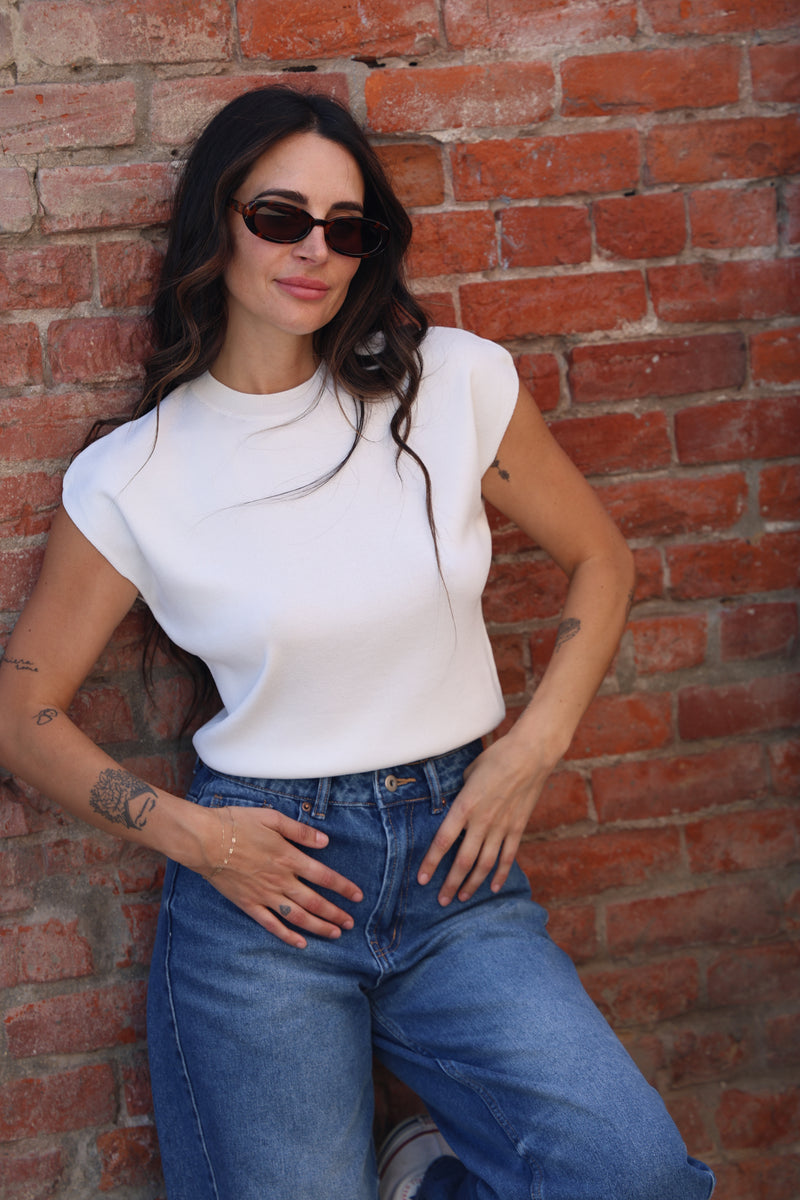 Woman lying on a brick floor wearing sunglasses and a white top.