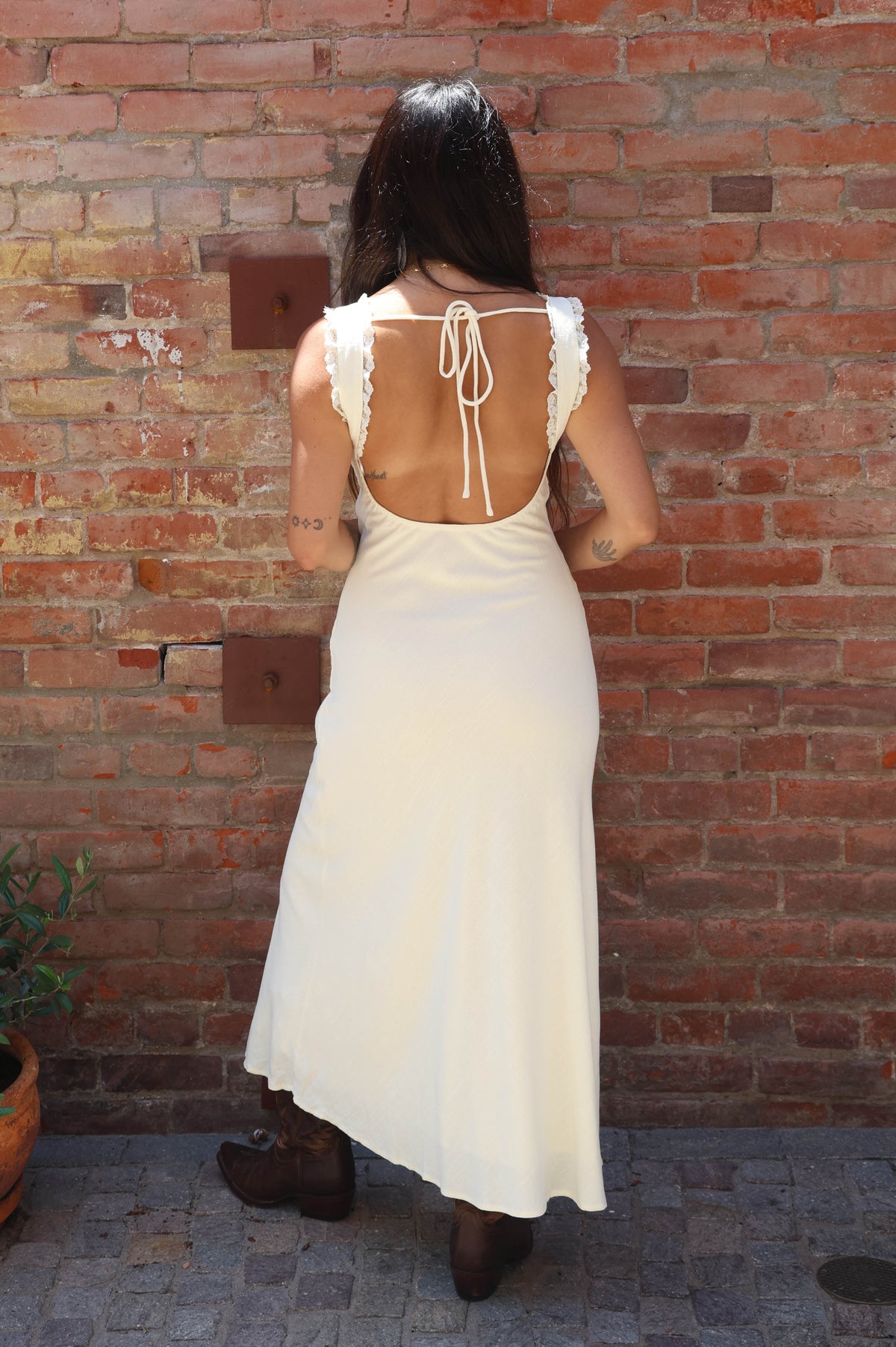 Woman wearing a white dress with lace straps against a brick wall.