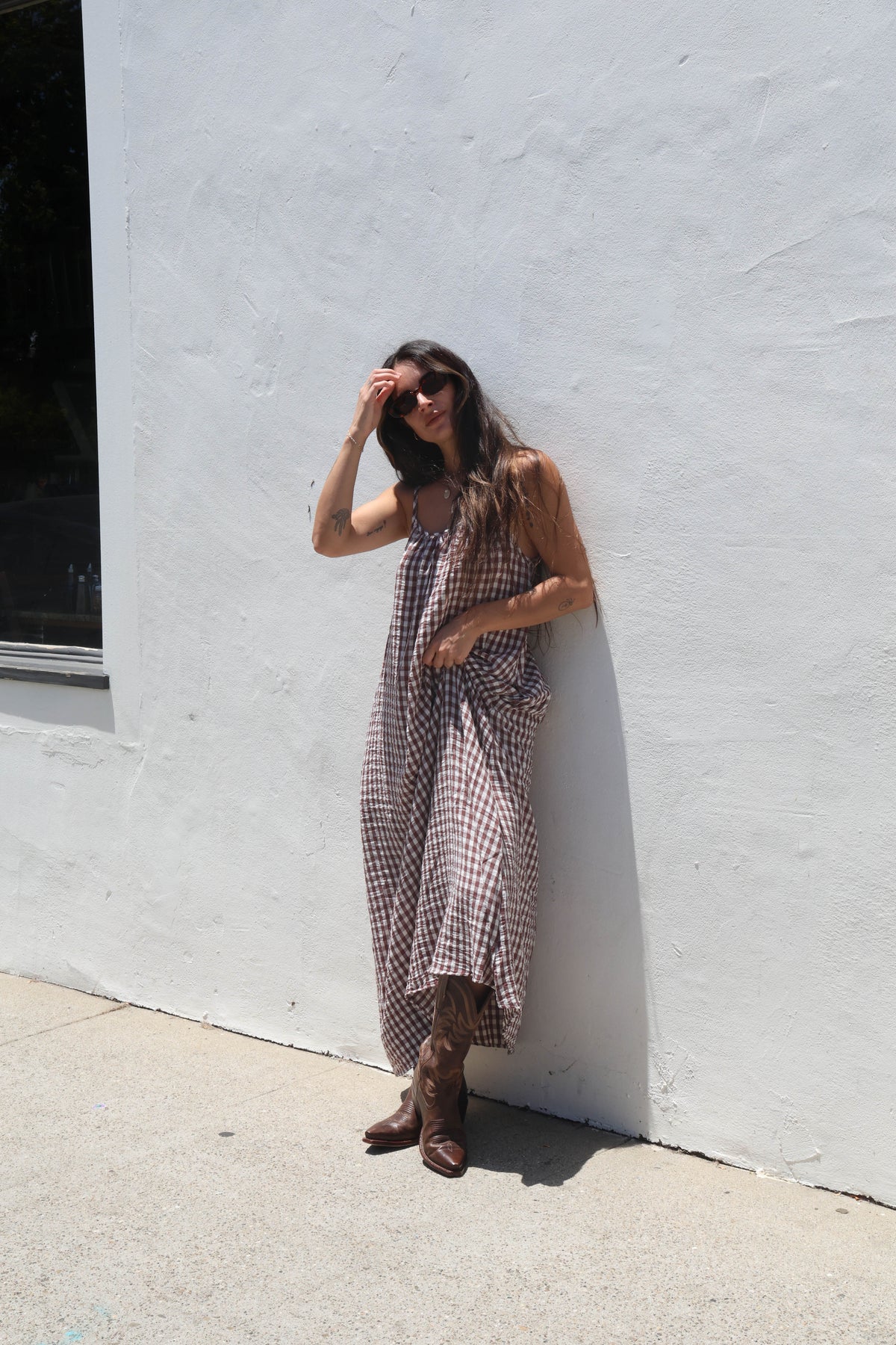 Woman in a plaid dress standing against a white wall.