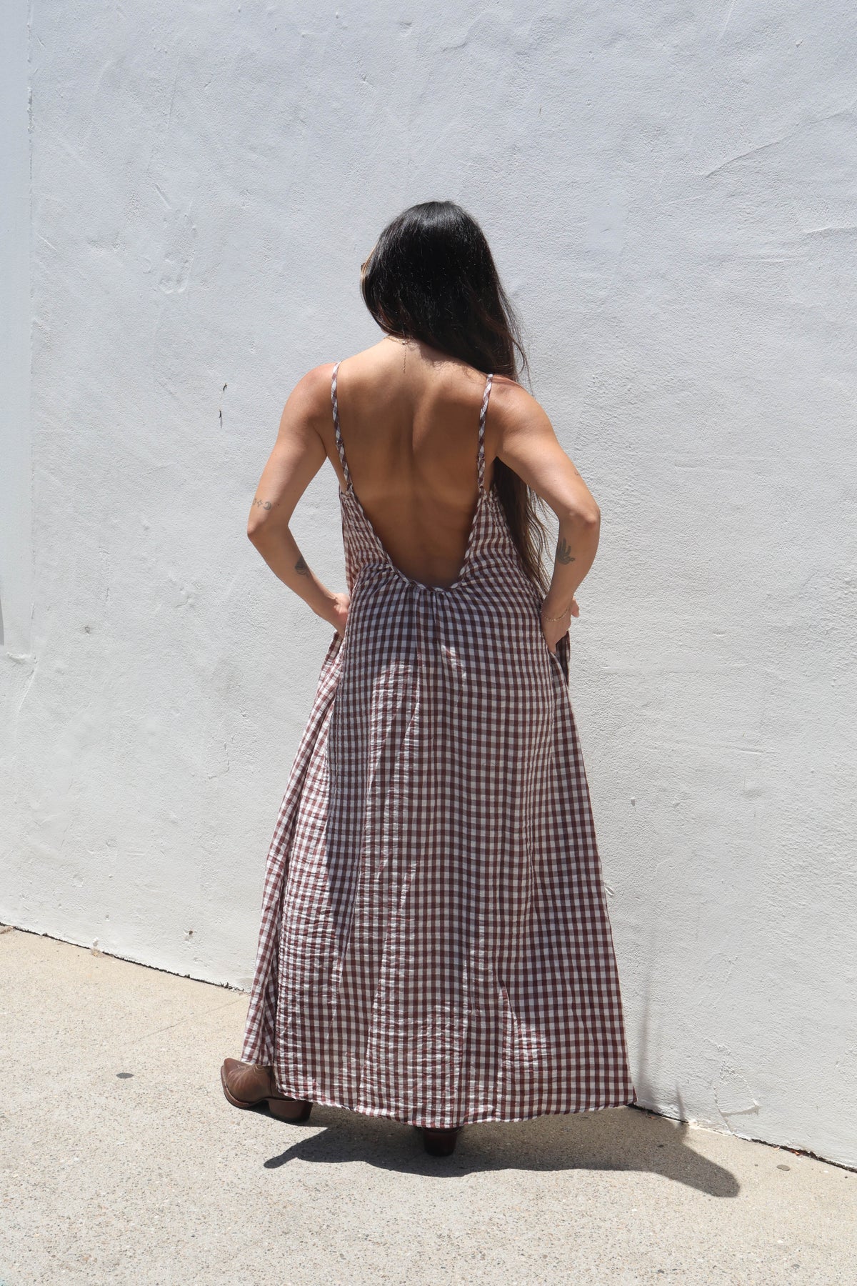 Woman wearing a checkered dress with an open back against a white wall.