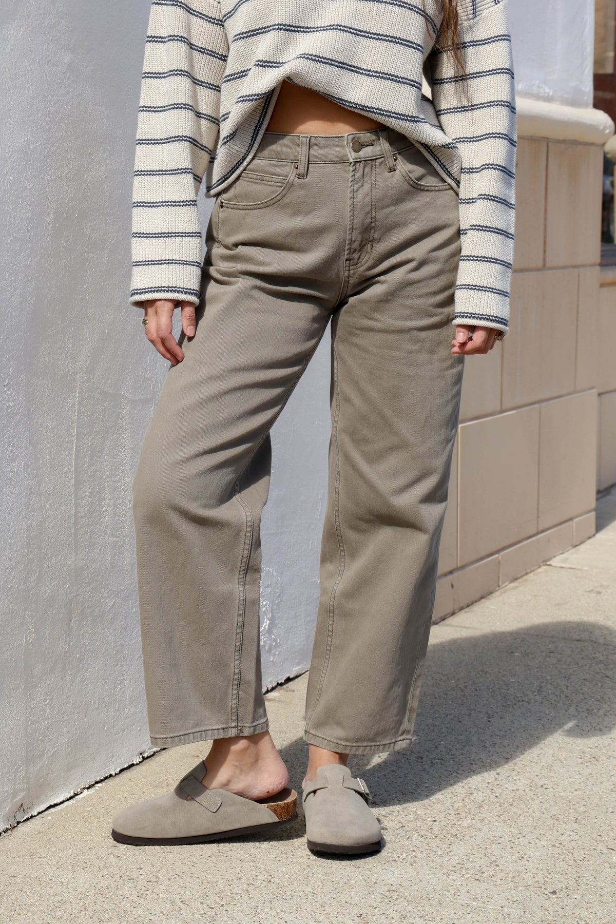 Woman wearing olive pants with a cream and blue striped sweater.