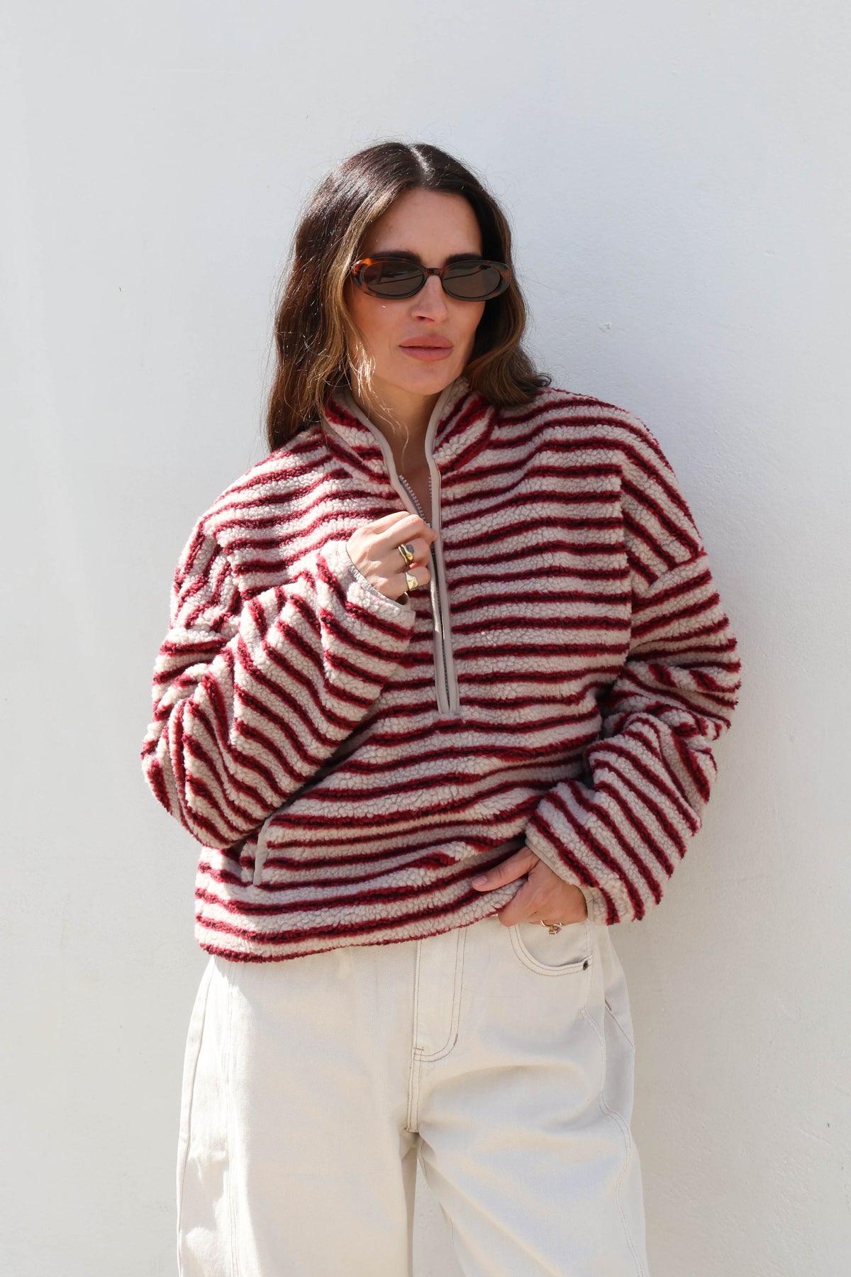 Woman wearing a striped cream and red fleece, sunglasses and white jeans.
