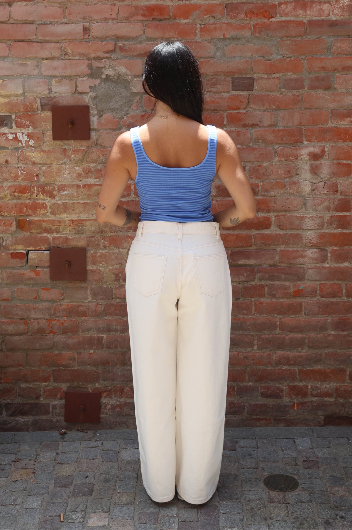 Person wearing a blue top and white pants standing against a brick wall.