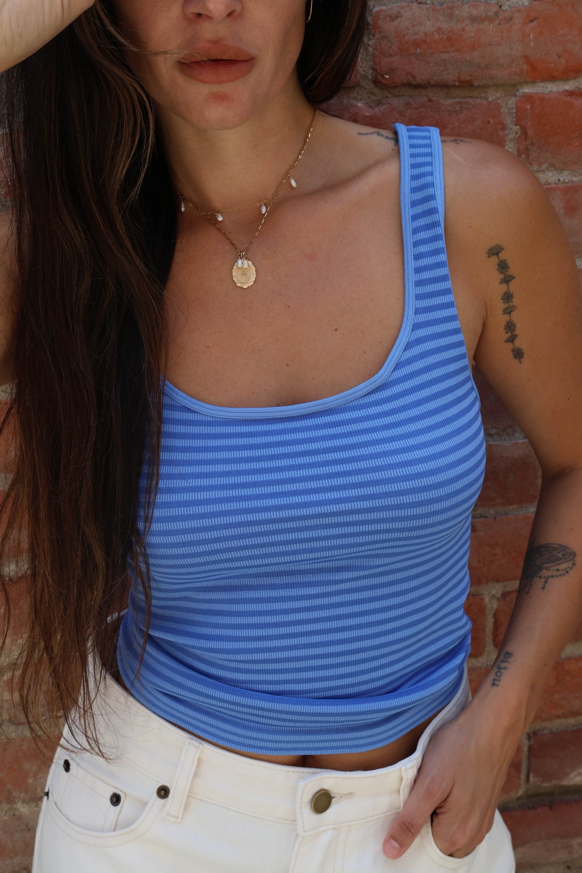 Person wearing a blue striped tank top against a brick wall.