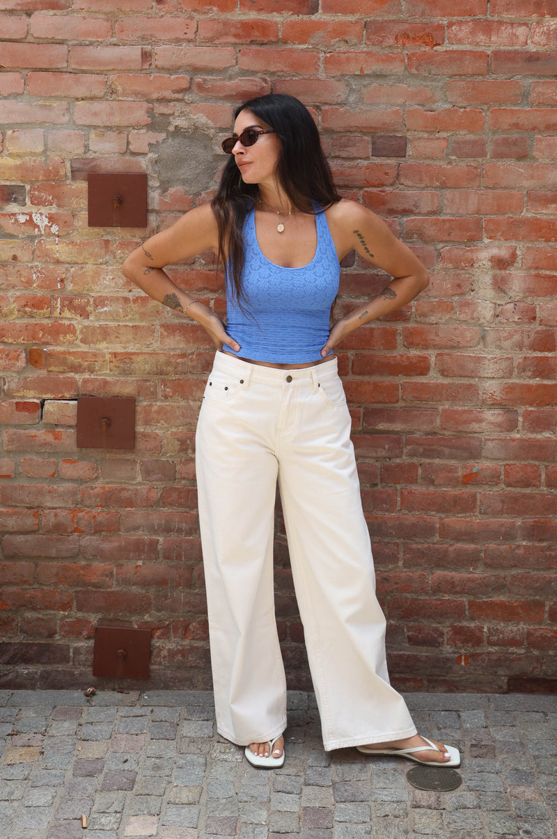 Woman in blue top and white pants standing against a brick wall.