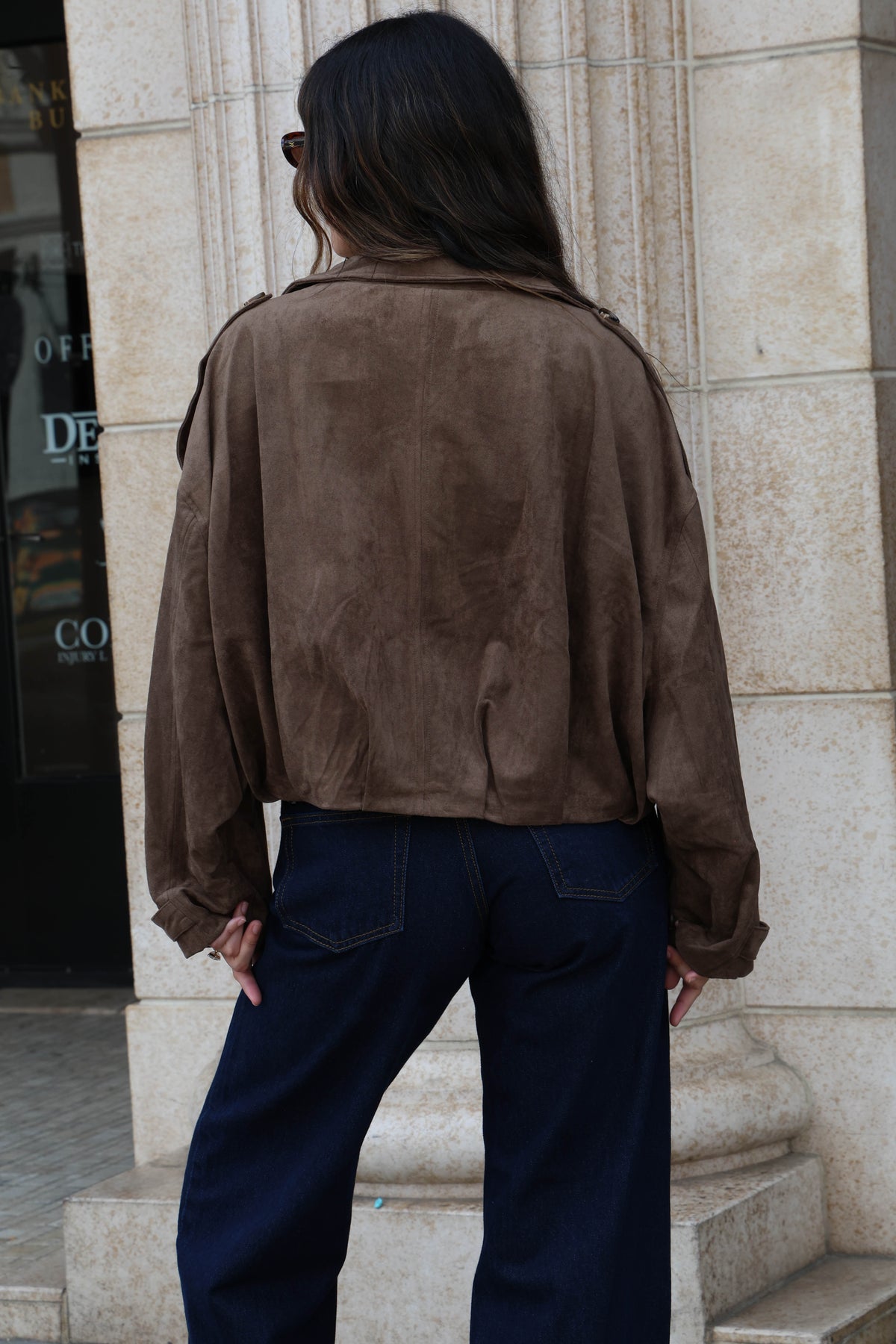 Woman wearing a brown suede jacket and dark jeans.
