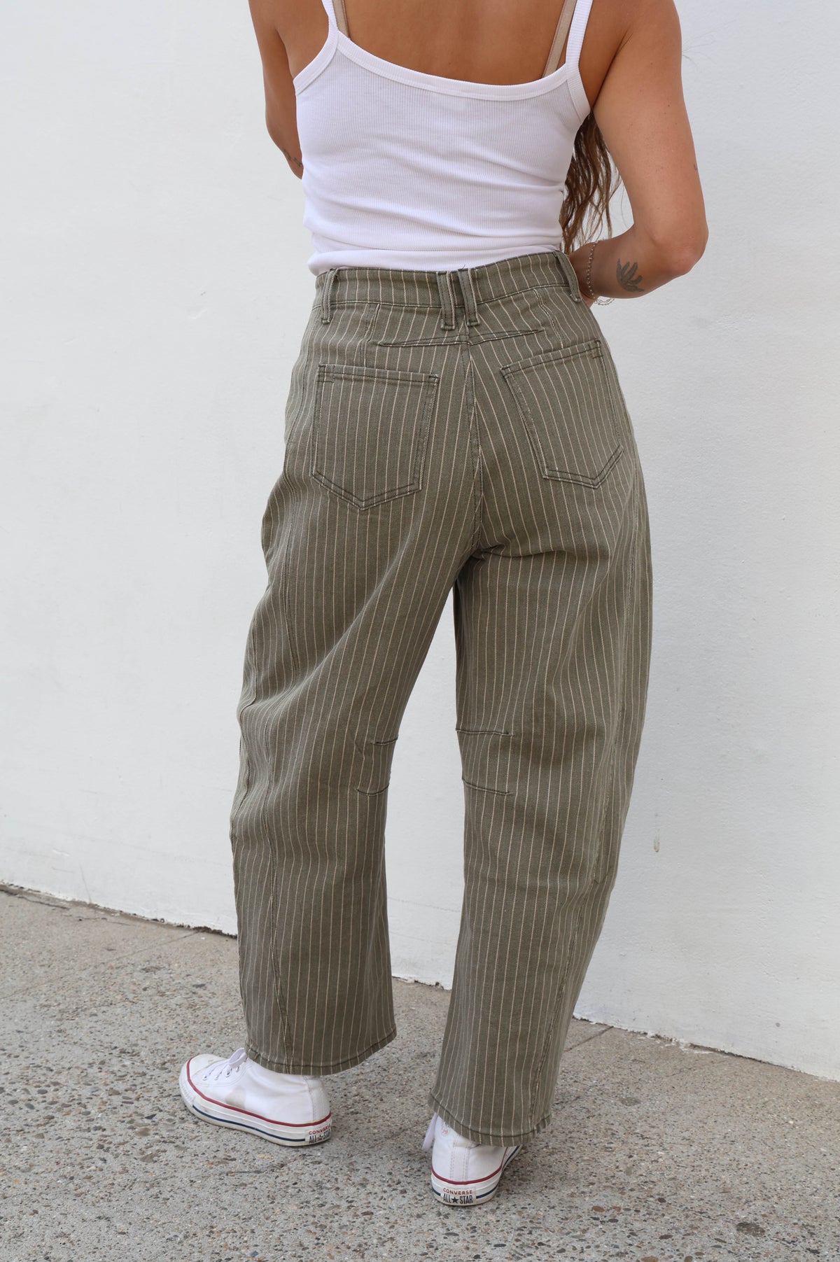 Woman wearing striped olive pants against a plain wall.