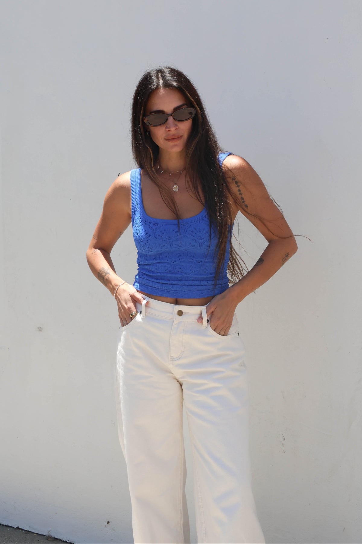 Woman wearing a blue top and white pants against a white wall