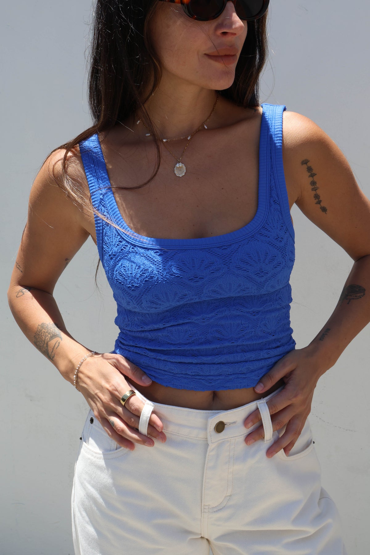 Woman wearing a blue tank top and white pants against a gray background