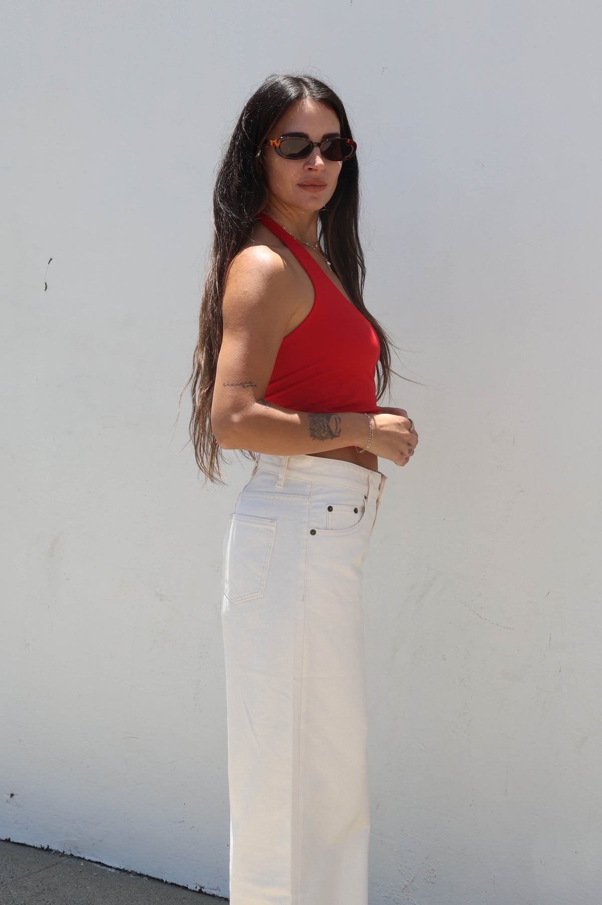 Woman wearing a red top and white pants against a white wall