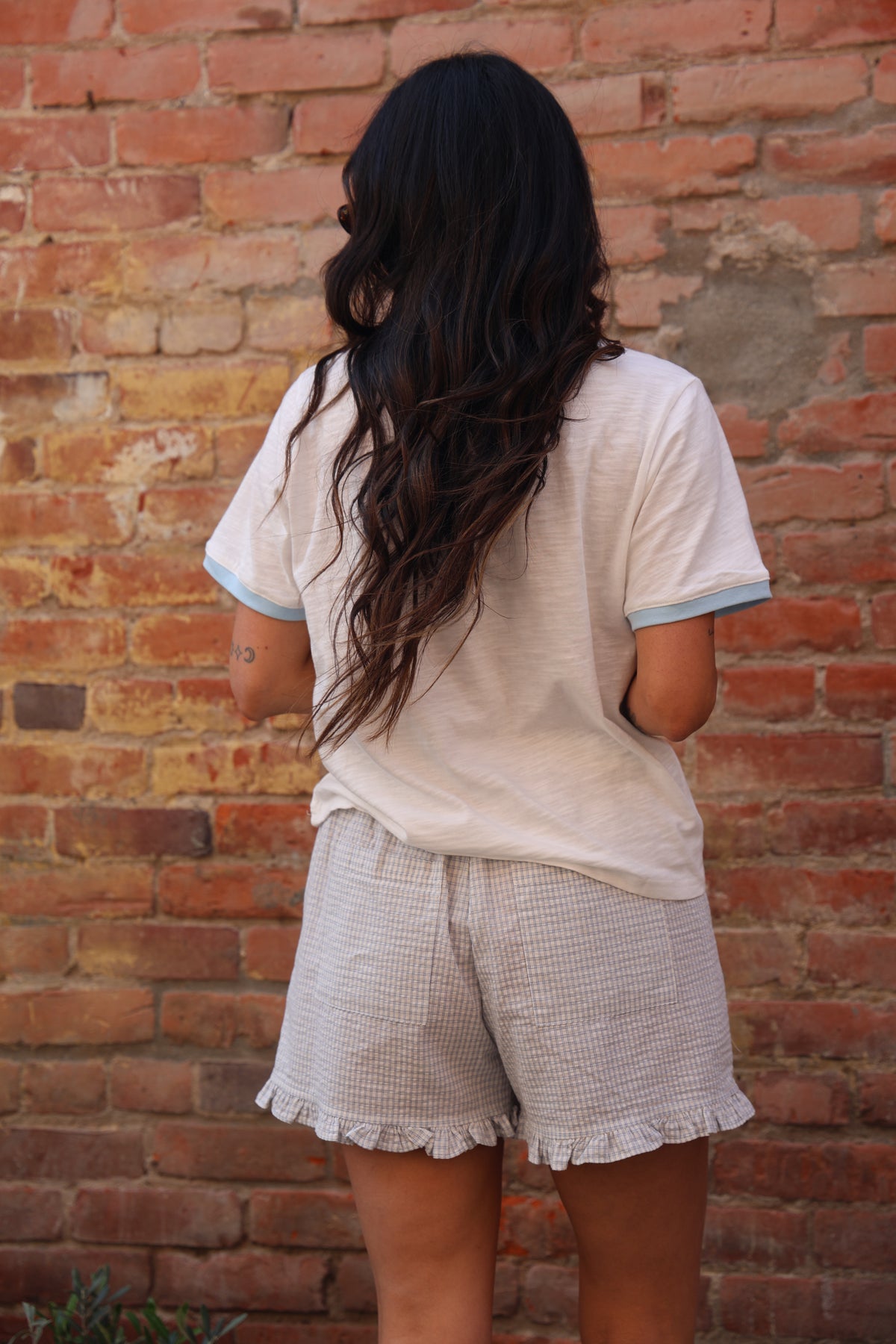 Person wearing a light-colored outfit against a brick wall