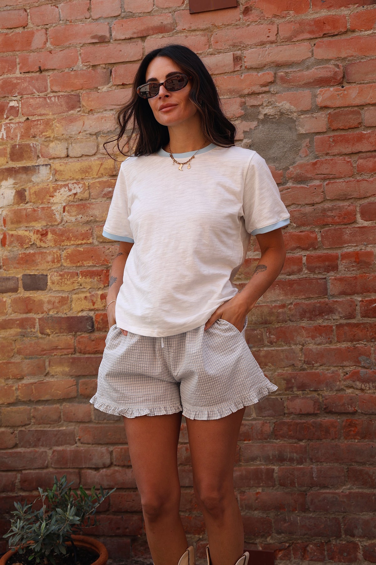 Woman wearing a white t-shirt and light-colored shorts against a brick wall.