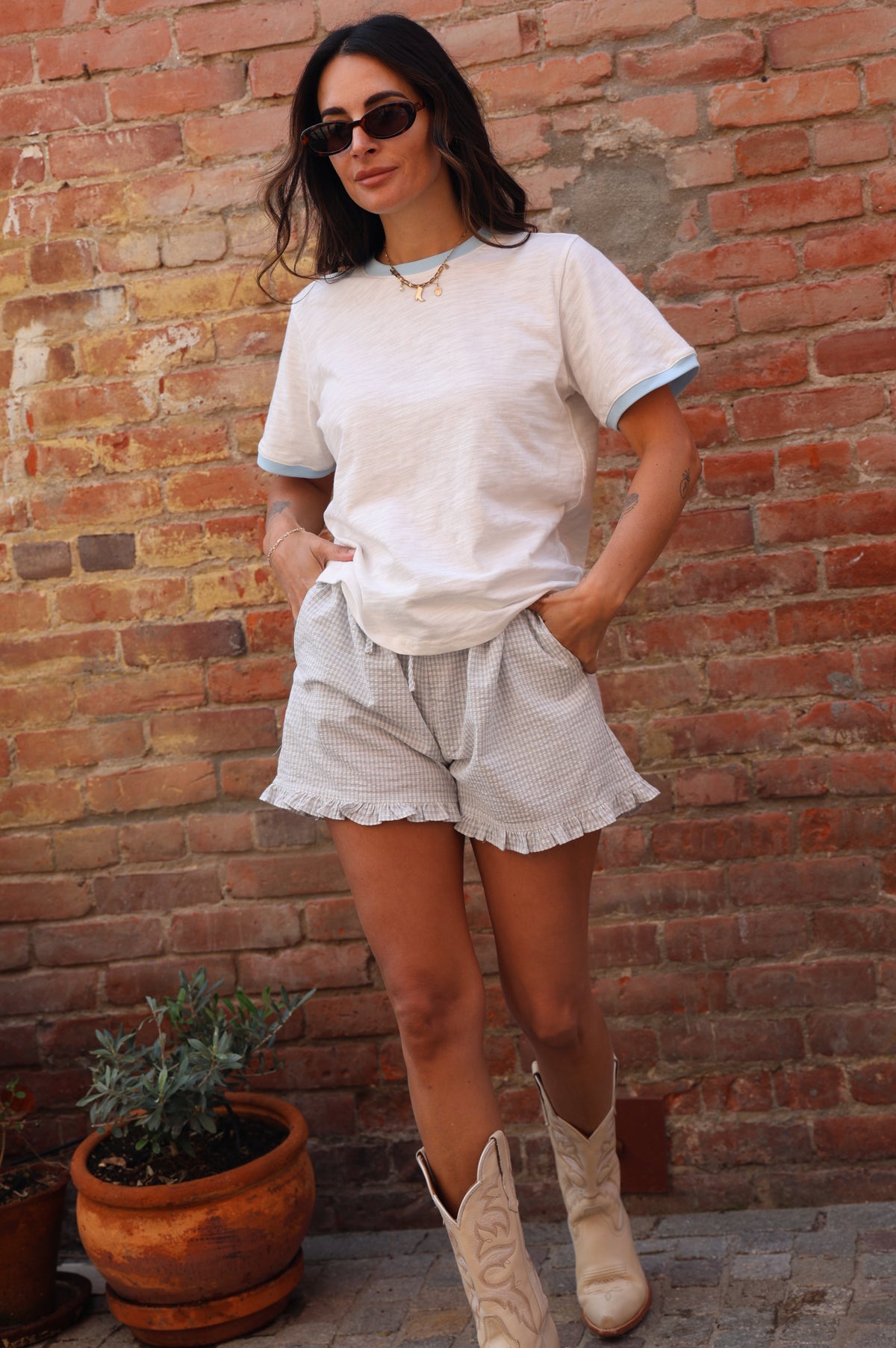 Woman in a white outfit standing on a brick pavement with a plant in the background