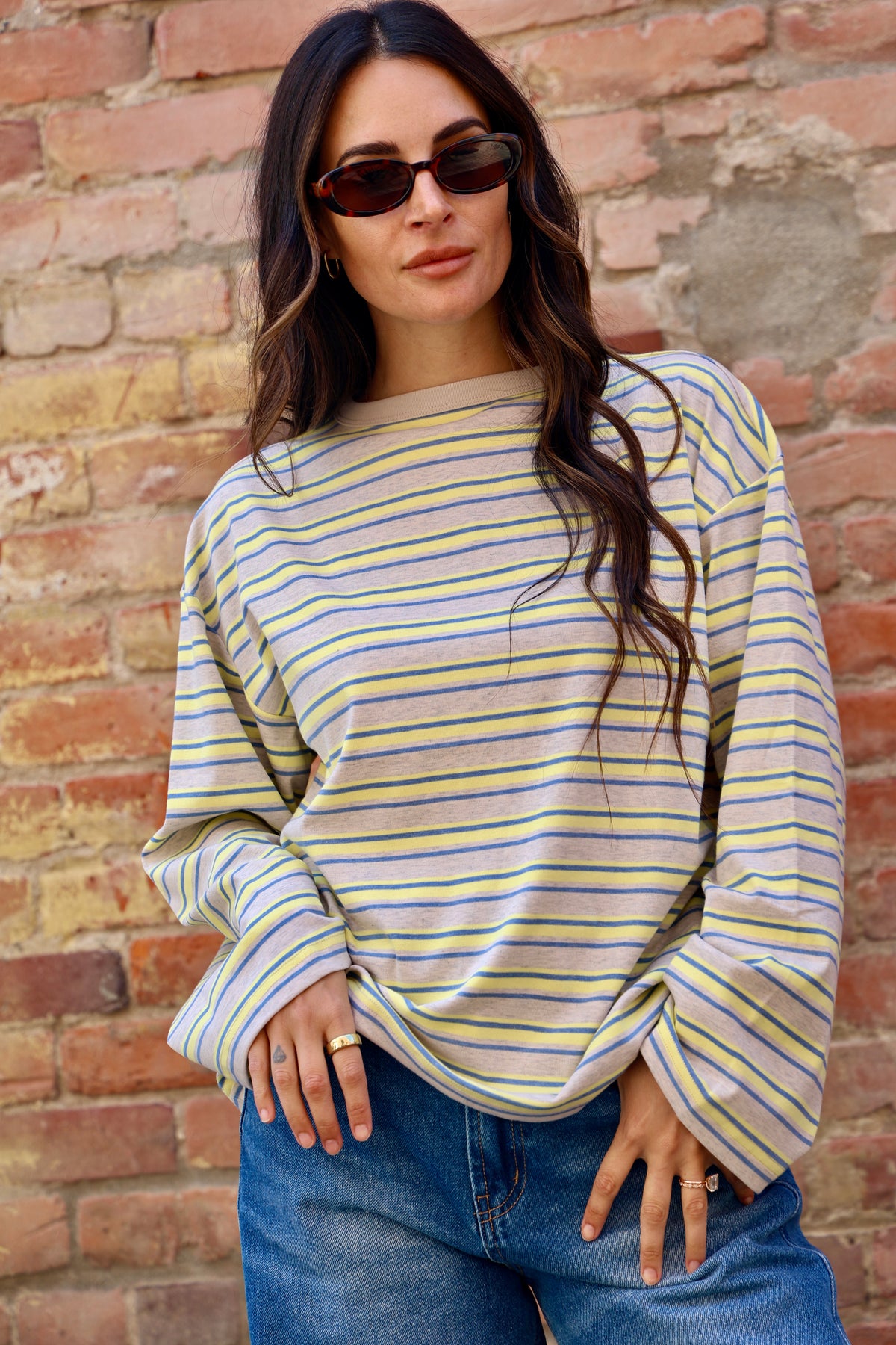 Woman wearing a striped long-sleeve top and sunglasses against a brick wall.