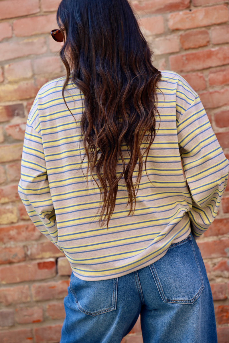 Person wearing a yellow and blue striped shirt and blue jeans against a brick wall.