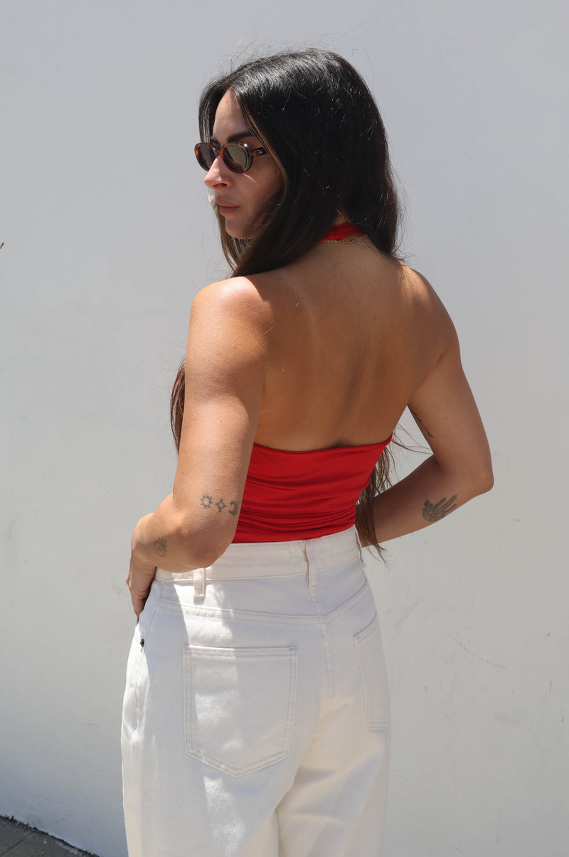 Woman wearing a red top and white pants against a white wall