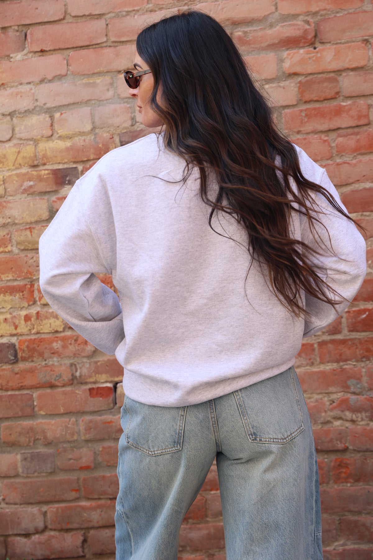 Person wearing a beige hoodie and blue jeans against a brick wall