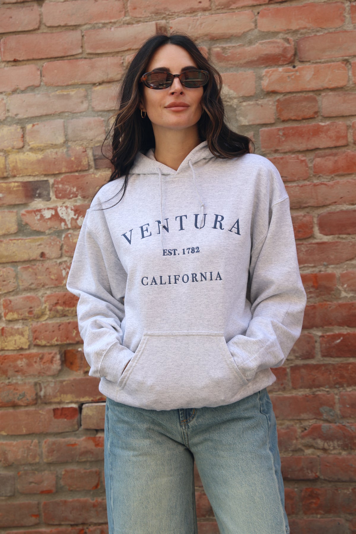 Person wearing a gray hoodie with 'Ventura California' text against a brick wall.