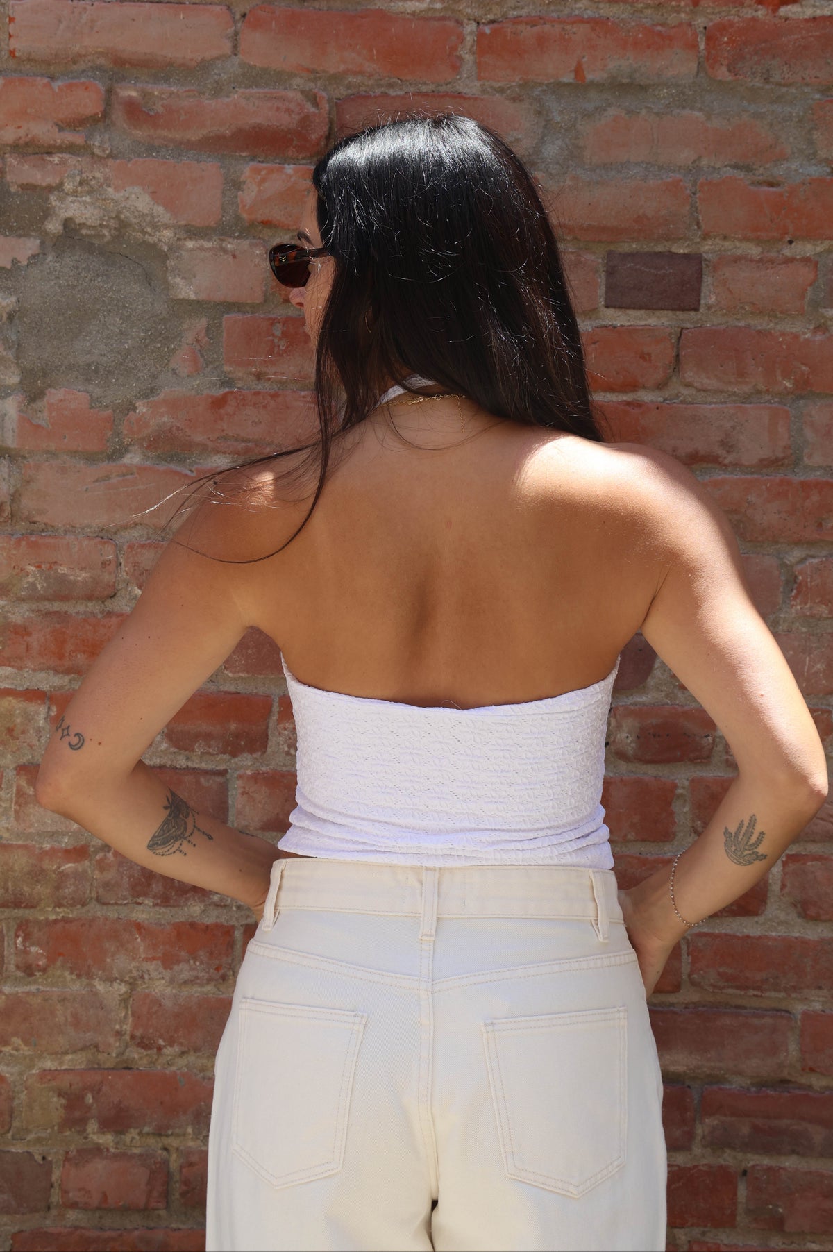 Person wearing a white top and beige pants against a brick wall