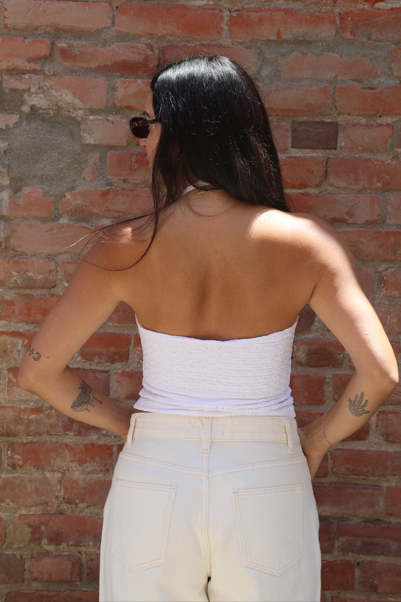 Person wearing a white top and beige pants against a brick wall