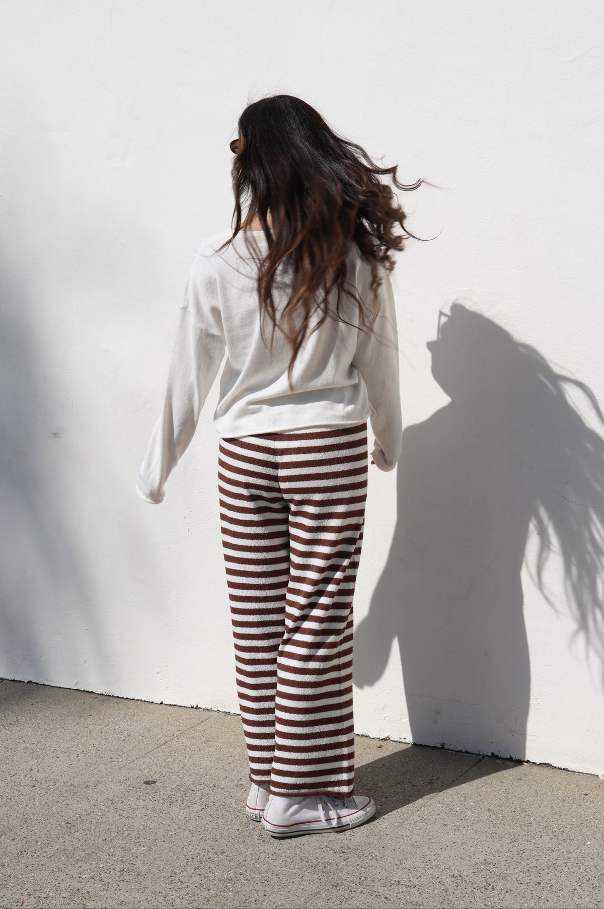 Person wearing a white shirt and striped pants standing against a white wall.