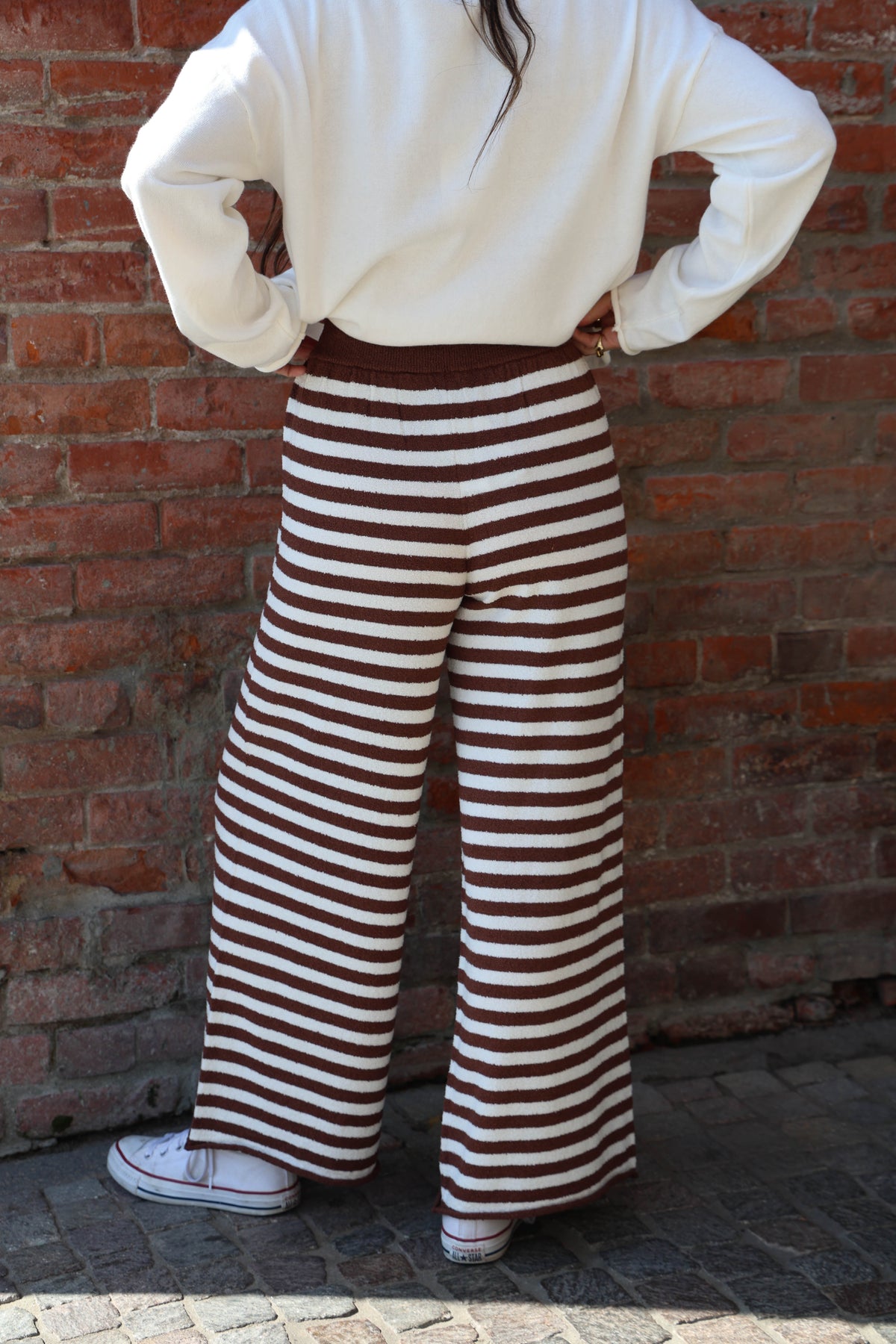 Person wearing brown and white striped pants against a brick wall.