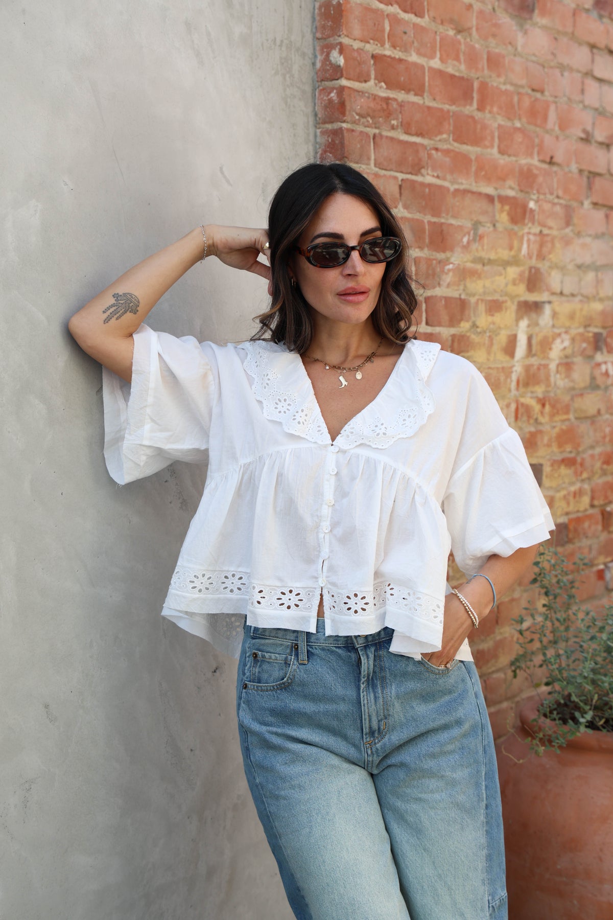 Woman wearing a white blouse and blue jeans leaning against a wall.