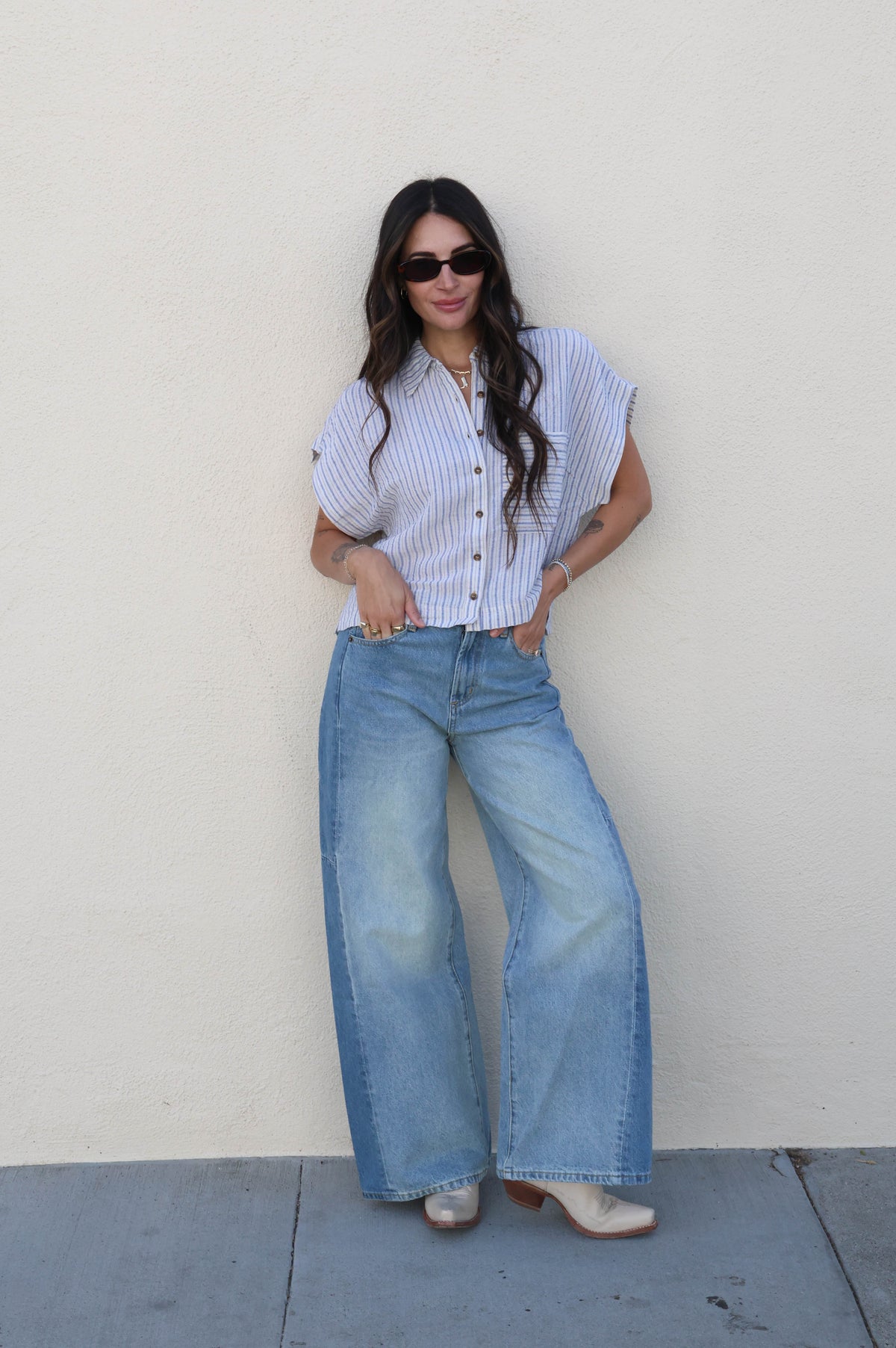 Woman wearing a striped shirt and wide-leg jeans against a plain wall.