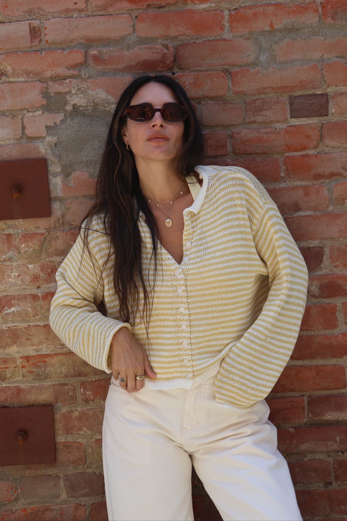 Woman wearing a striped shirt and sunglasses against a brick wall.