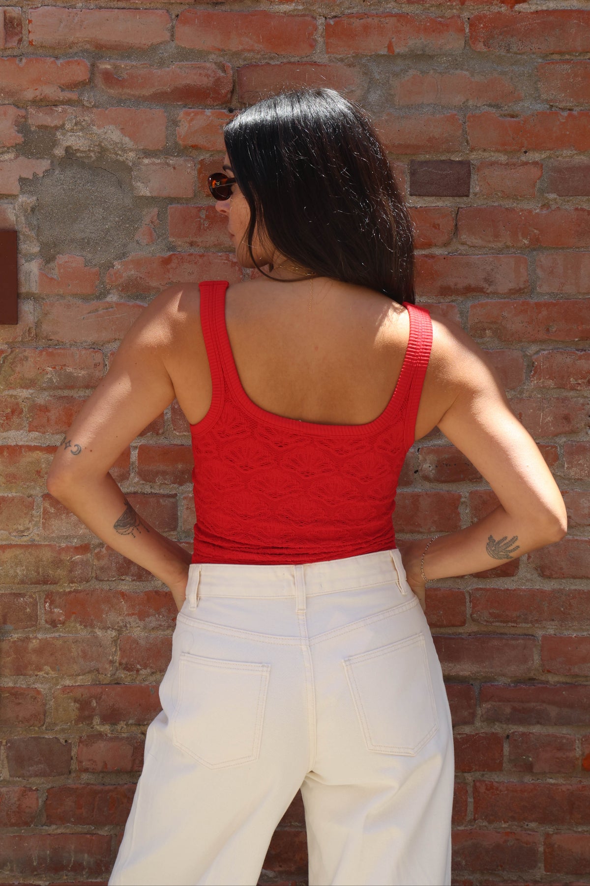 Person wearing a red top and white pants against a brick wall