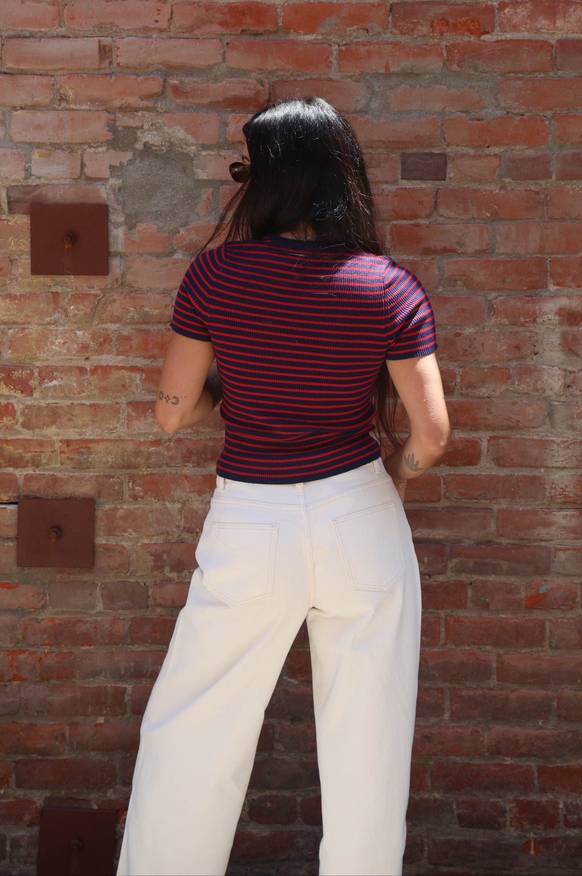 Person wearing a striped shirt and white pants standing against a brick wall.