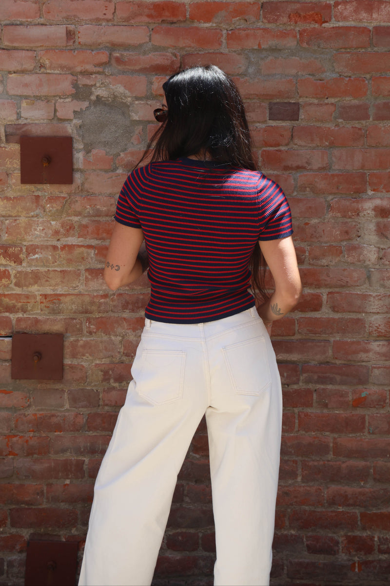 Person wearing a striped shirt and white pants standing against a brick wall.