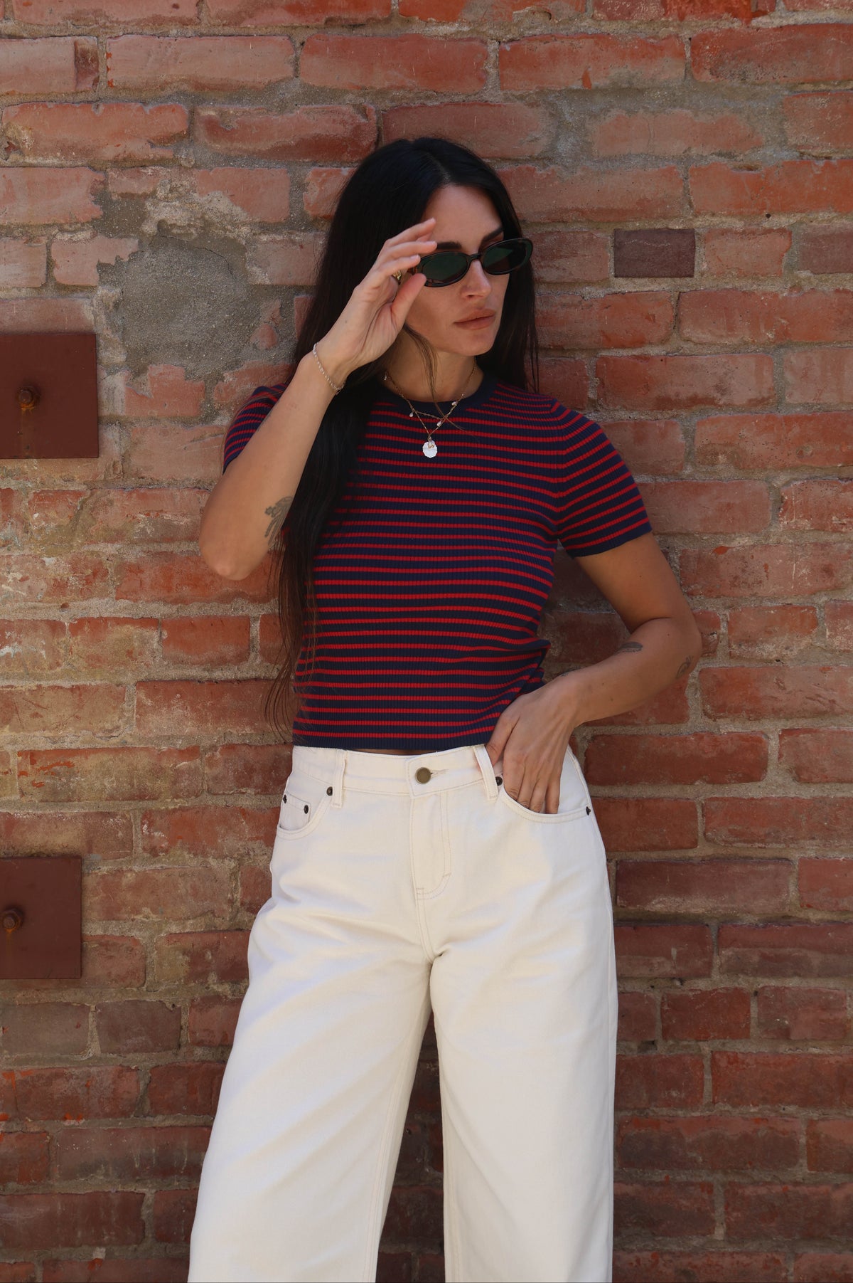 Woman wearing a striped shirt and white pants against a brick wall.