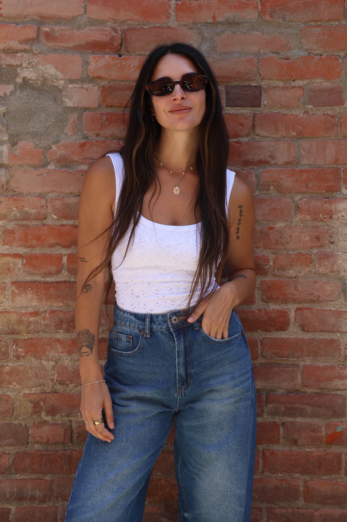 Woman wearing sunglasses and a white top against a brick wall